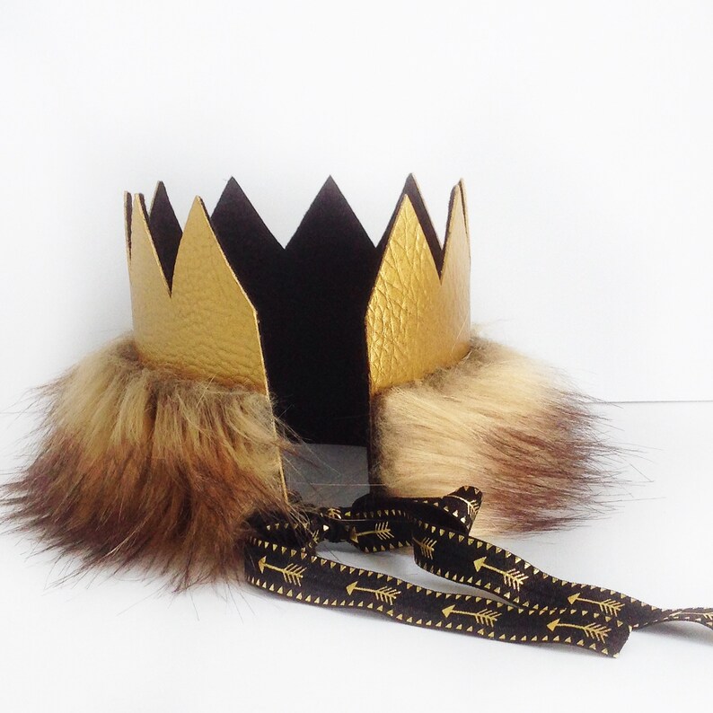 May include: A gold crown with black felt and faux fur trim. The crown is tied with a black ribbon with gold arrow accents.