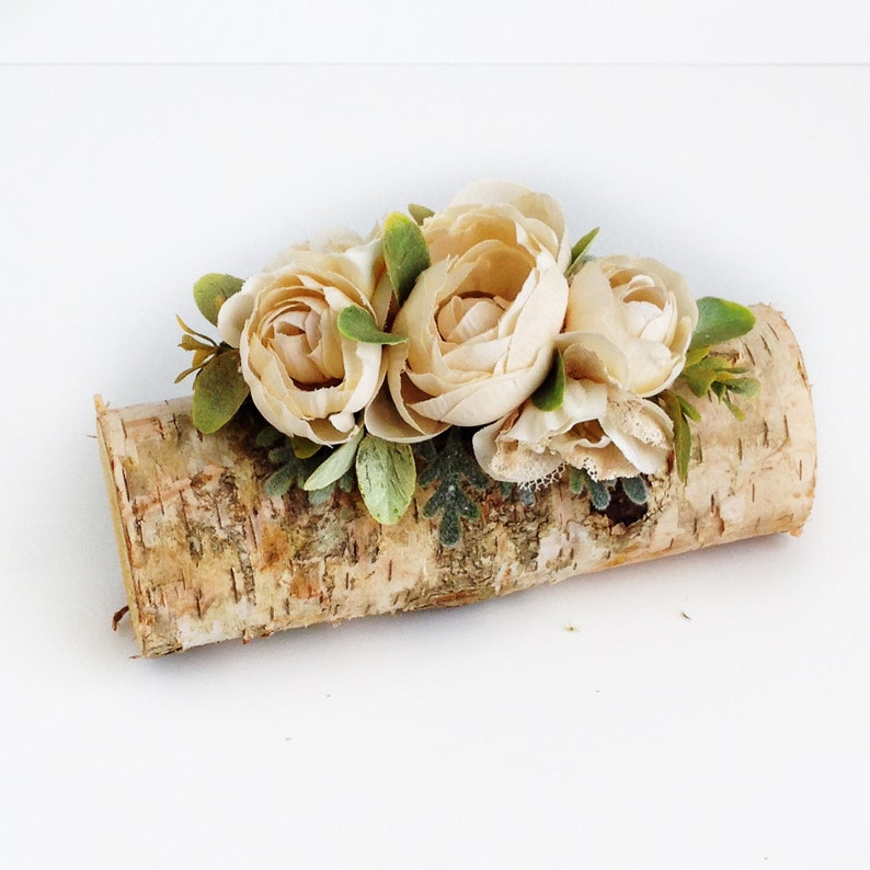 May include: A small log of birch bark with a cluster of cream-colored artificial flowers and green leaves.