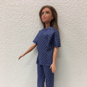 May include: A blue and white patterned doll outfit with a short-sleeved top and pants. The outfit is made for a doll with long brown hair.