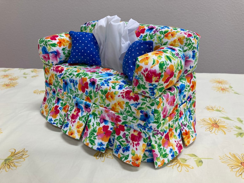 Op de afbeelding: Een tissueboxhoes met bloemenpatroon in de vorm van een bank met blauwe en witte stippen kussens.