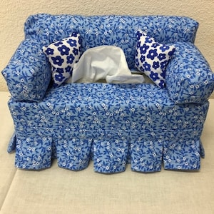 Op de afbeelding: Een blauwe en witte tissueboxhoes met bloemenpatroon in de vorm van een bank met twee kussens. De kussens hebben een witte achtergrond met blauwe bloemen.