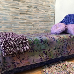 May include: A purple and blue twin-sized bed with a floral patterned bedspread and a purple knitted throw blanket. The headboard is made of blue tiles and there are two purple pillows on the bed.