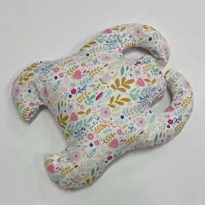 Può includere: Un cuscino bianco con un motivo floreale in tonalità rosa, giallo e blu. Il cuscino ha la forma di un granchio con due grandi chele.