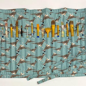 Peut inclure: Un étui enroulable en tissu bleu sarcelle avec un motif d'oiseaux. L'étui comporte 18 fentes pour ranger les pinceaux. L'étui est doté d'une sangle marron avec une boucle.