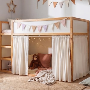 May include: A wooden loft bed with a ladder, white curtains, and a play area underneath. The room is decorated with a giraffe toy, pillows, and a rug. A string of lights and a banner add a cozy touch.