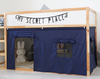 May include: A wooden loft bed with a navy blue fabric enclosure, featuring a window and rolled-up curtains. The bed frame has a ladder and shelves. A banner above the enclosure reads "MY SECRET PLACE". A stuffed bunny and star-shaped pillow are visible inside.
