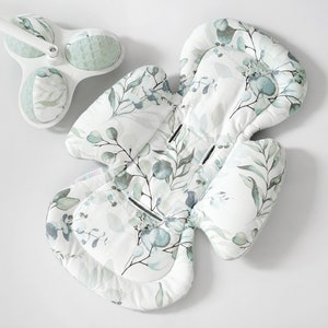 Op de afbeelding: Een witte babystoel met een groen bloemenpatroon. De stoel heeft een hoofdsteun en een lichaamsondersteuning.