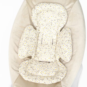 Op de afbeelding: Een beige baby schommelstoel met een uitneembare, gevoerde inzet met een wit en geel bloemenpatroon.