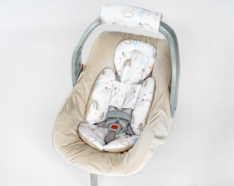 Könnte beinhalten: Ein beiger Babyautositz mit einer weißen und blauen gemusterten Innenausstattung mit Bergen, Regenbögen und Sternen. Der Sitz hat einen grauen Fünf-Punkt-Gurt.