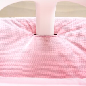 Op de afbeelding: Close-up van een roze stoffen stoelkussen met een wit frame. De stof heeft een textuurpatroon.