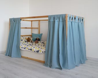 May include: A wooden bed frame with light blue curtains draped around it. The bed is made with a white and yellow patterned bedding and has a stuffed animal on top.