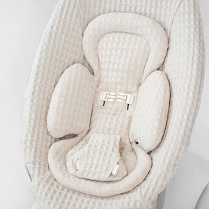 Op de afbeelding: Een beige baby wipstoel met een wafelstructuur. De wipstoel heeft een gevoerde hoofdsteun en een vijfpunts gordel.