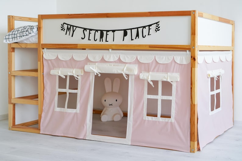 May include: A wooden bunk bed with a pink tent-like canopy. The canopy has white scalloped trim and two white windows. The bed has a shelf on the side and a banner that reads "My Secret Place".