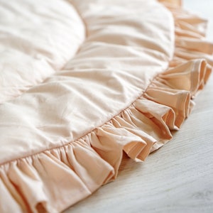 May include: A pale pink round play mat with a ruffled edge. The mat is made of soft fabric and is perfect for babies and toddlers.