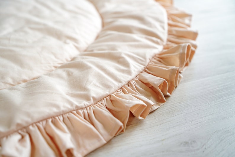 May include: A pale pink round play mat with a ruffled edge. The mat is made of soft fabric and is perfect for babies and toddlers.