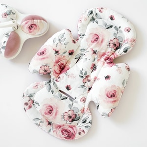 Op de afbeelding: Een baby-autostoel inzetstuk en hoofdsteun met een bloemenpatroon van roze rozen en grijze bladeren op een witte achtergrond. De hoofdsteun heeft een roze mesh-gedeelte. De set is ontworpen voor babycomfort en ondersteuning.