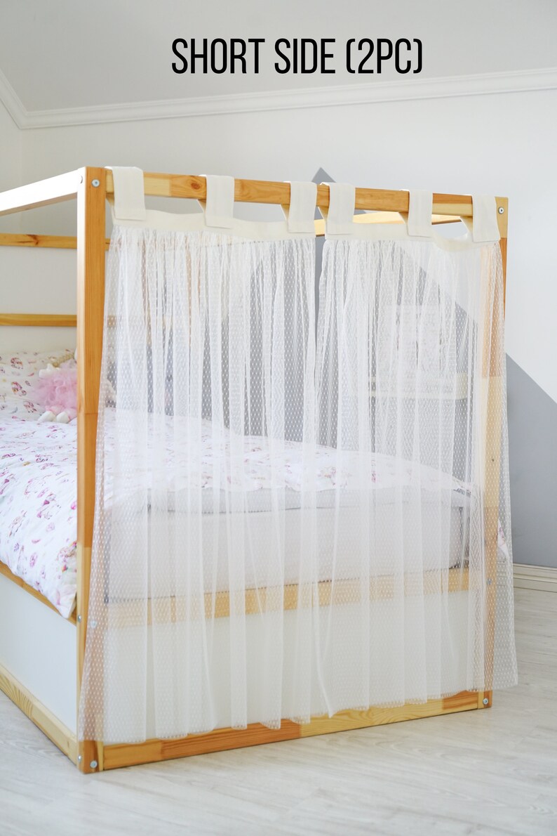 May include: A set of two white sheer curtains with a dotted pattern, hanging from a wooden bed frame. The curtains are labeled "SHORT SIDE (2PC)".