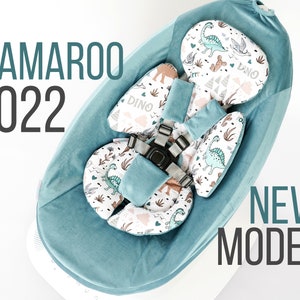 Puede incluir: Un columpio para bebé azul turquesa con un inserto de tela estampado con dinosaurios blancos y verdes. El columpio tiene un arnés de cinco puntos y el texto "MAMAROO 2022 NEW MODEL" es visible en la imagen.