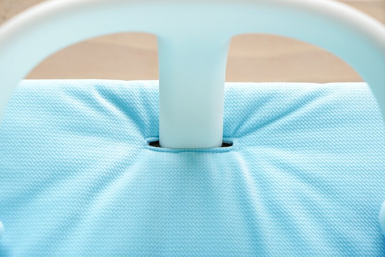 Pu&ograve; includere: Primo piano di una sedia in tessuto blu chiaro con una struttura in plastica bianca. Il tessuto ha una trama testurizzata.