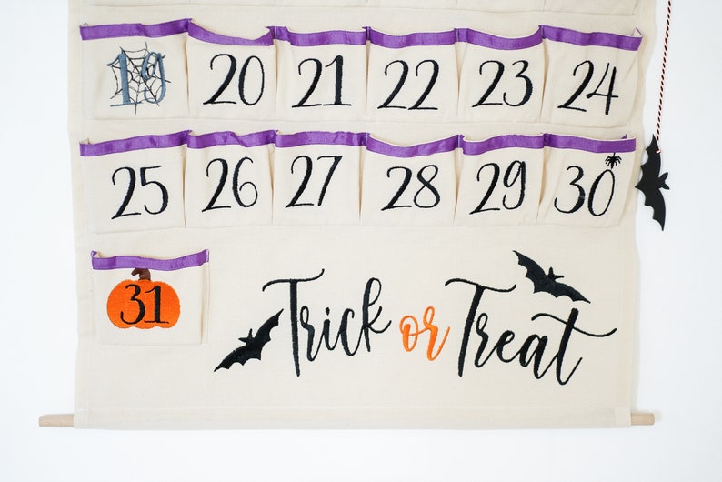 May include: A cream-colored Halloween advent calendar with numbered pockets, purple trim, and a wooden dowel. Features a pumpkin, bats, and the phrase "Trick or Treat". Includes numbers 19-31.