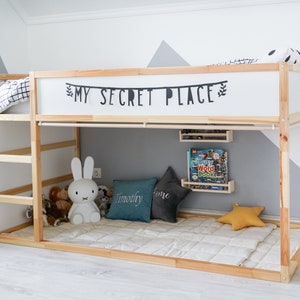 Puede incluir: Una litera de madera con un colch&oacute;n blanco y una s&aacute;bana blanca. La litera superior tiene un letrero que dice "My Secret Place". Hay animales de peluche y almohadas en el suelo debajo de la cama.
