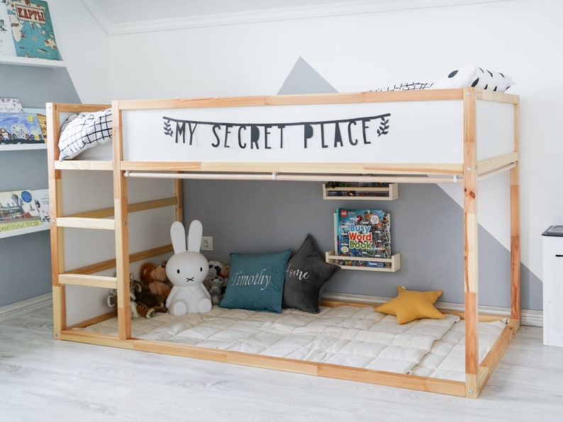Puede incluir: Una litera de madera con un colch&oacute;n blanco y una s&aacute;bana blanca. La litera superior tiene un letrero que dice "My Secret Place". Hay animales de peluche y almohadas en el suelo debajo de la cama.