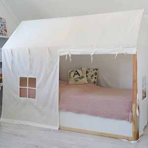 May include: A white canvas tent-like structure built over a bed frame. The tent has a small window and is tied with white strings. The bed has a pink and white checkered bedspread and two pillows with green and white patterns.