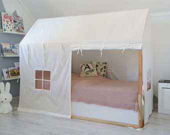 Könnte beinhalten: Ein weißes Zelt aus Segeltuch, das über einem Bettrahmen gebaut ist. Das Zelt hat ein kleines Fenster und ist mit weißen Schnüren gebunden. Das Bett hat eine rosa-weiß karierte Bettdecke und zwei Kissen mit grün-weißen Mustern.