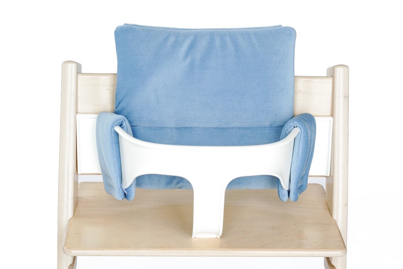 May include: A light wood high chair with a blue cushion and a white safety bar. The chair has a light blue padded backrest and seat inserts. The safety bar is white and T-shaped.