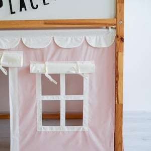 May include: A pink fabric canopy with white scalloped trim and two white fabric window coverings. The canopy is attached to a wooden bed frame.