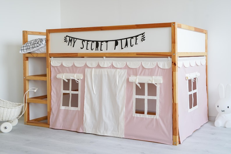 May include: A wooden bunk bed with a pink and white tent-like canopy. The canopy has two windows and a white curtain in the middle. The bed has a wooden ladder and a shelf on the side. The top of the bed has a sign that says "My Secret Place".