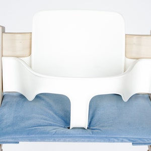 May include: A white high chair with a blue cushion. The chair has a wooden frame and a white plastic seat and backrest. The blue cushion is rectangular and fits in the seat of the chair.