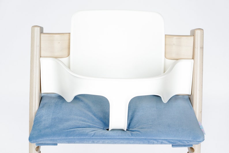 May include: A white high chair with a blue cushion. The chair has a wooden frame and a white plastic seat and backrest. The blue cushion is rectangular and fits in the seat of the chair.