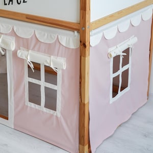 May include: A pink and white fabric canopy with scalloped edges and white trim. The canopy has two windows with white frames and a white fabric valance. The canopy is attached to a wooden bed frame.