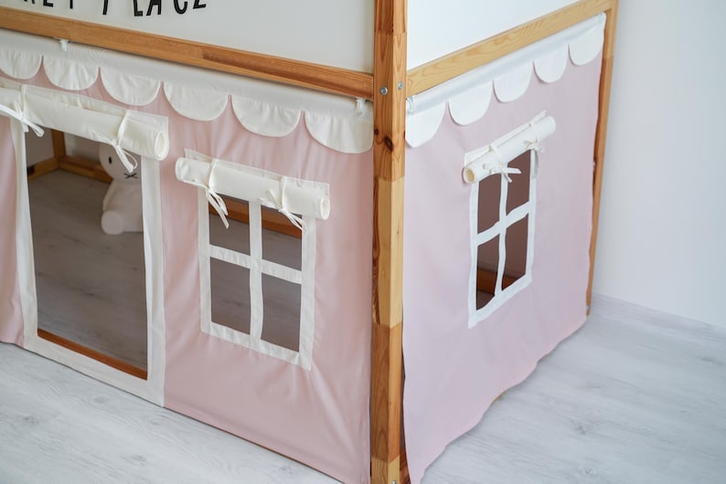 May include: A pink and white fabric canopy with scalloped edges and white trim. The canopy has two windows with white frames and a white fabric valance. The canopy is attached to a wooden bed frame.