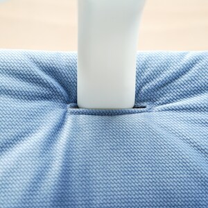 May include: Close-up of a light blue textured fabric, possibly upholstery, with a white object inserted into a slit. The fabric has a woven pattern, and the lighting creates shadows.