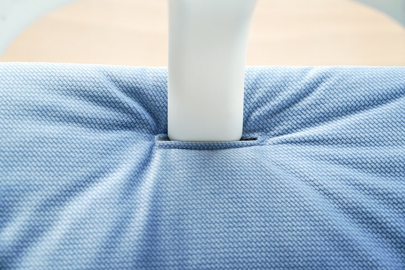 May include: Close-up of a light blue textured fabric, possibly upholstery, with a white object inserted into a slit. The fabric has a woven pattern, and the lighting creates shadows.