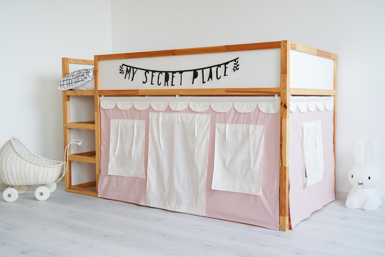 May include: A wooden loft bed with a pink fabric canopy and white curtains. The bed has a shelf on the side and a black banner that reads "My Secret Place".