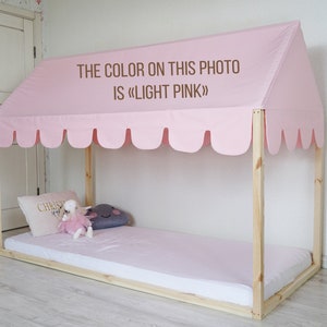 K&ouml;nnte beinhalten: Ein Holzbettgestell mit einem rosa Baldachin und einer rosa Matratze. Der Baldachin hat einen gewellten Rand und der Text "THE COLOR ON THIS PHOTO IS &laquo;LIGHT PINK&raquo;" ist darauf gedruckt.