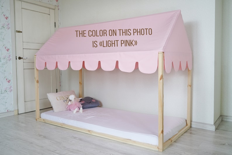 K&ouml;nnte beinhalten: Ein Holzbettgestell mit einem rosa Baldachin und einer rosa Matratze. Der Baldachin hat einen gewellten Rand und der Text "THE COLOR ON THIS PHOTO IS &laquo;LIGHT PINK&raquo;" ist darauf gedruckt.