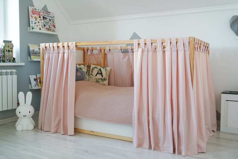 May include: A wooden bed frame with pink curtains draped around it. The bed has a pink and white checkered bedding and two pillows with a letter A and a gray animal design.