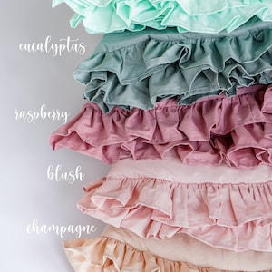 May include: Five ruffled pillowcases in different colors, stacked on top of each other. The colors are mint, eucalyptus, raspberry, blush, and champagne.