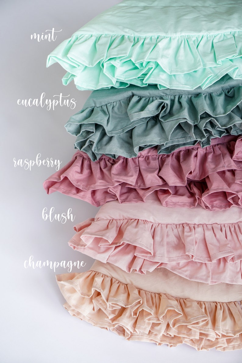 May include: Five ruffled pillowcases in different colors, stacked on top of each other. The colors are mint, eucalyptus, raspberry, blush, and champagne.