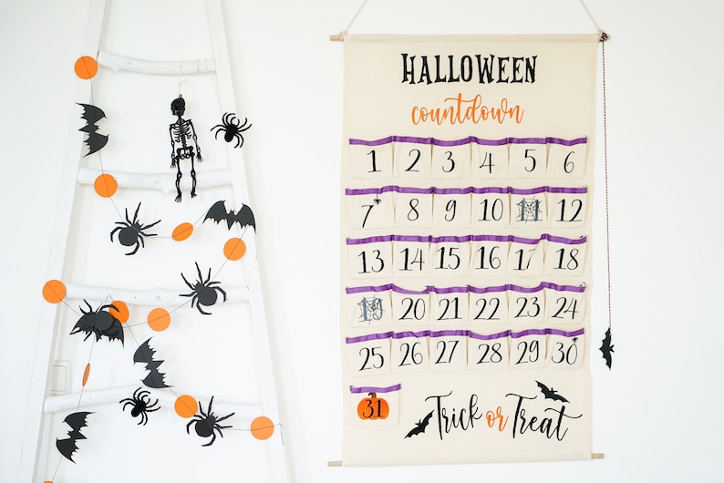 May include: A Halloween countdown calendar with pockets numbered 1-30, and the words "Halloween countdown" and "Trick or Treat". A garland of orange circles, black bats, and spiders hangs on a white ladder.