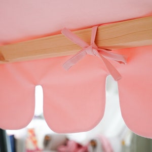 K&ouml;nnte beinhalten: Ein rosa Stoffbaldachin mit gewellten R&auml;ndern ist an einem Holzrahmen befestigt. Der Stoff ist in der Mitte mit einer Schleife gebunden.