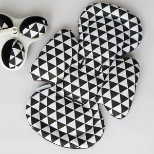 Op de afbeelding: Zwarte en witte babyzitverkleiner met geometrisch patroon. De verkleiner is gevormd als een grote, afgeronde driehoek met twee kleinere afgeronde driehoeken aan beide zijden.