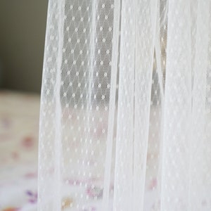 May include: White sheer curtain with small white polka dots. The curtain is made of a delicate fabric and has a soft, romantic feel.