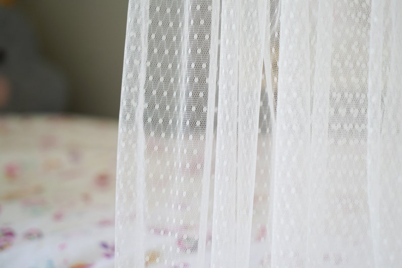 May include: White sheer curtain with small white polka dots. The curtain is made of a delicate fabric and has a soft, romantic feel.