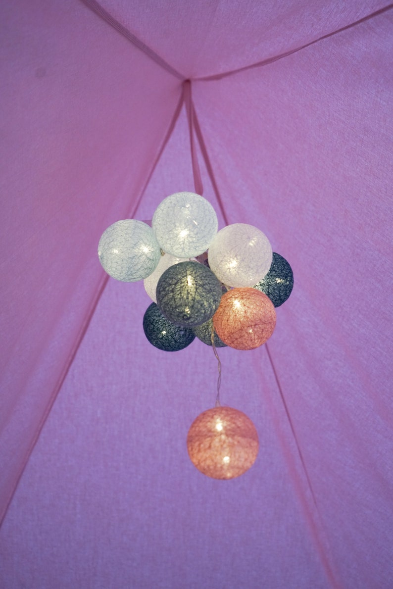 May include: A cluster of spherical string lights hanging inside a pink fabric tent. The illuminated globes feature a textured, woven thread design in shades of white, light blue, dark blue, and soft pink, creating a glowing decorative effect.