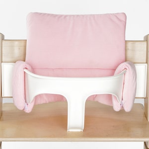 Op de afbeelding: Een roze gevoerd hoge stoel kussen met een witte lade. Het kussen is gemaakt van zachte stof en heeft een comfortabel ontwerp.
